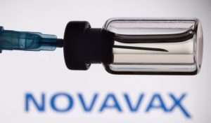 A vial and a syringe are seen in front of a displayed Novavax logo, in this illustration taken - TA NEA - TA NEA