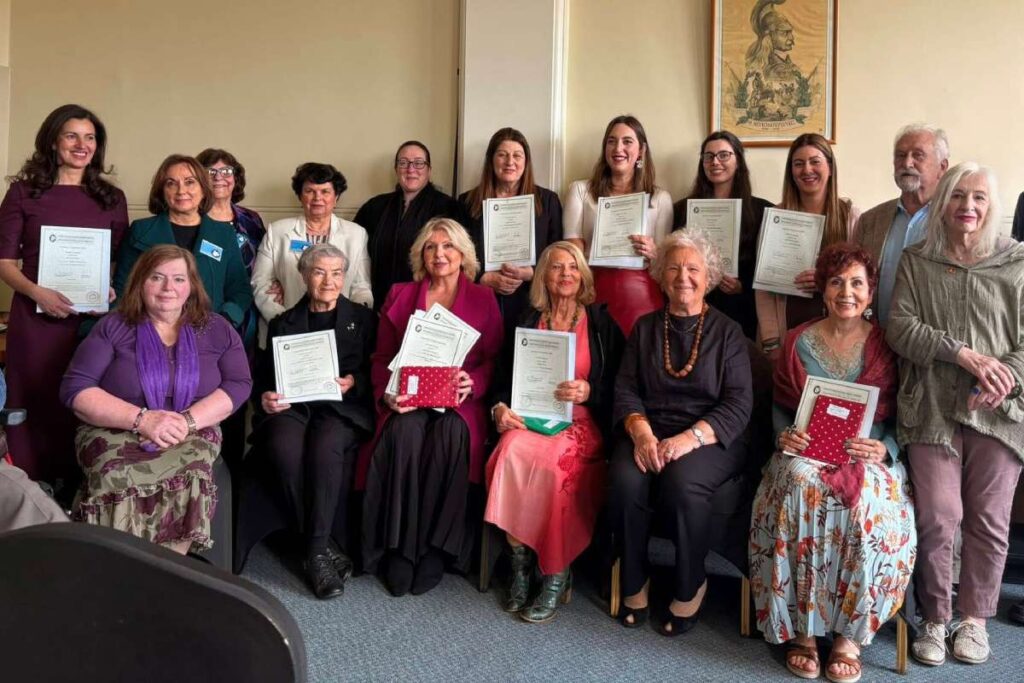 Group of adults posing with certificates at a ceremony, seated and standing in a room.