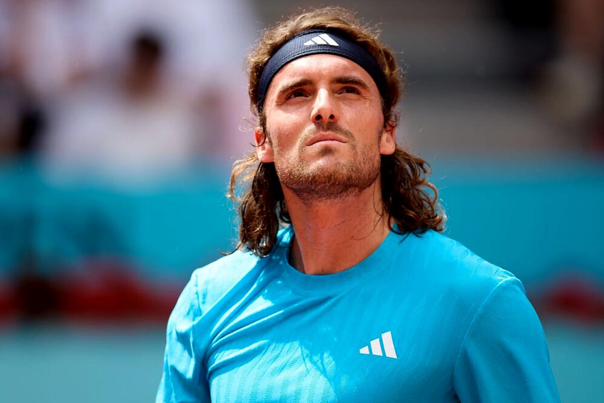 Male tennis player with long hair and a dark headband wearing a bright blue shirt, looking upward on a court