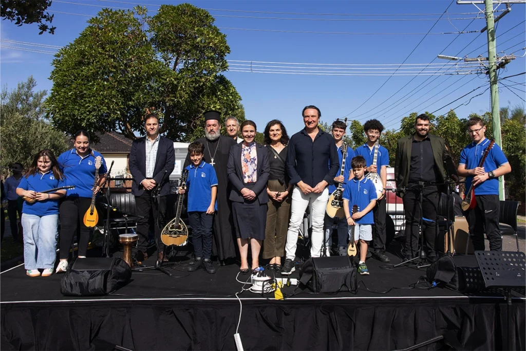 Group of adults and children on an outdoor stage with musical instruments, posing for a photo.
